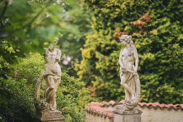 Due statue chiare nel verde di un giardino.