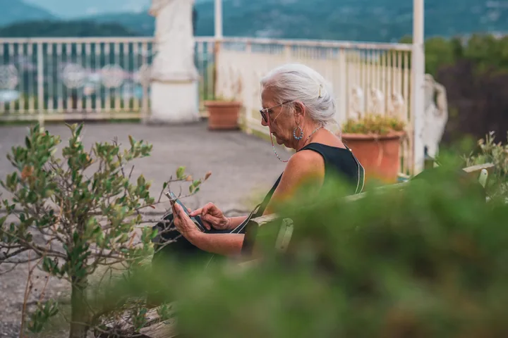 Una donna seduta in terrazza legge, tra le piante.