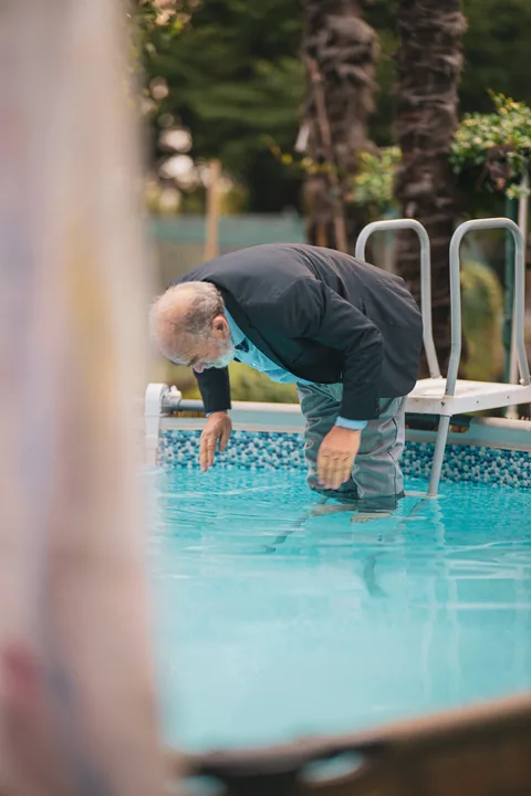 Gaetano si china verso l’acqua dal bordo della piscina.