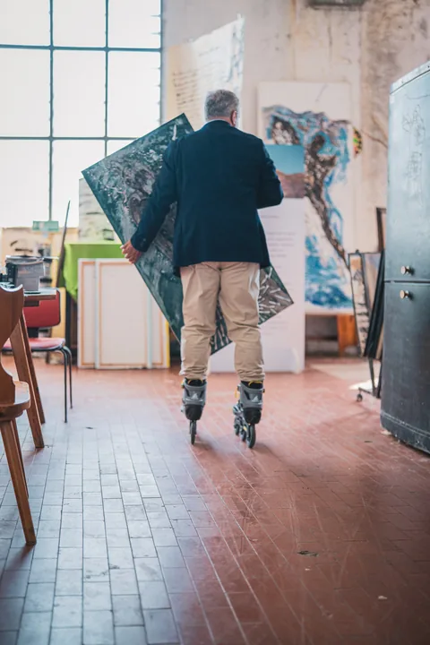 Una figura sui pattini attraversa l’atelier con una tela.