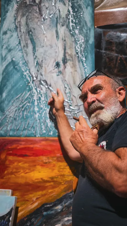 Gaetano accanto a una tela azzurra e arancione.