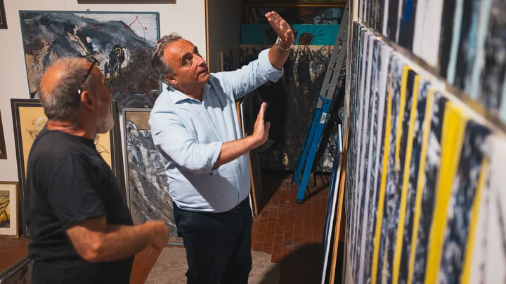 Due uomini discutono davanti alle tele nell’atelier.