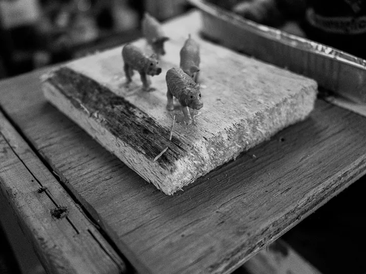 Piccole figure scolpite su un basamento, in bianco e nero.